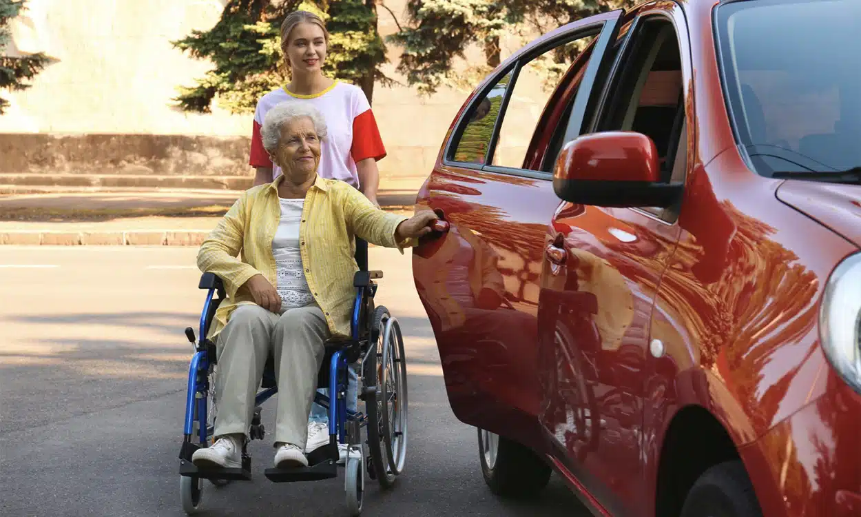 Taxi conventionné qui aide une veille femme en fauteuil roulant à rentrer dans la voiture