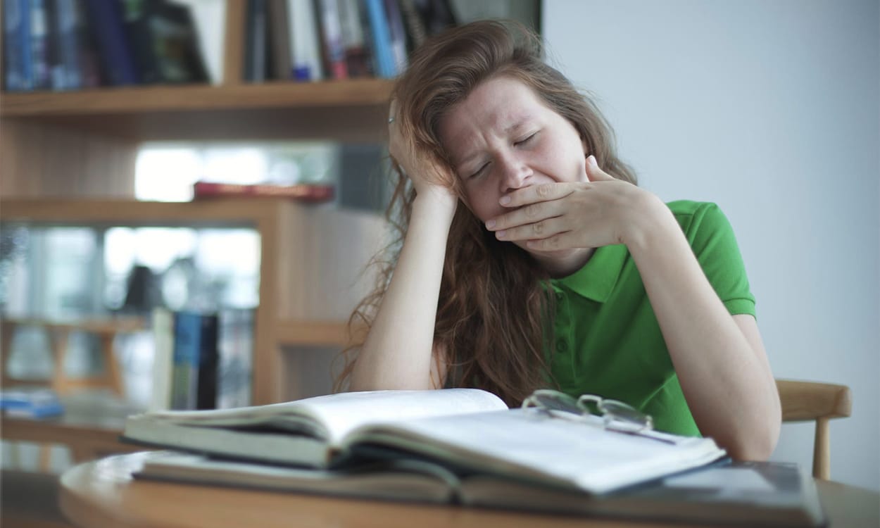 Une adolescente fatiguée qui baille devant ses cahiers de cours