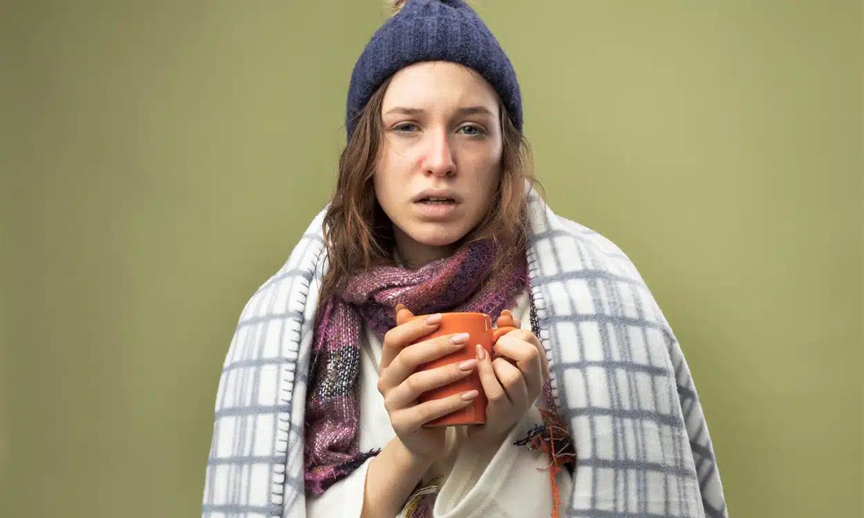 Femme malade avec un bonnet et une couverture tenant une tasse